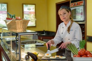 A chef preparing food in a kitchen with a basket of vegetables, a cutting board, and a bowl of tomatoes. - Hotel Krefelder Hof (Krefeld)