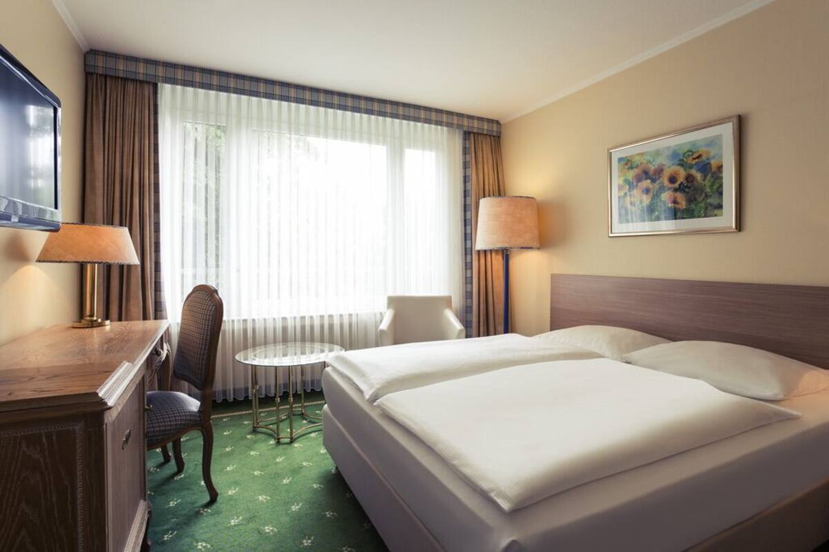 Ein Hotelzimmer mit einem Bett, zwei Sesseln, einem kleinen Tisch, einem Schreibtisch und einem Fernseher.