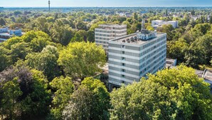 Een meerhoog gebouw, omringd door weelderige groene bomen, met een helder uitzicht op de omliggende stad.