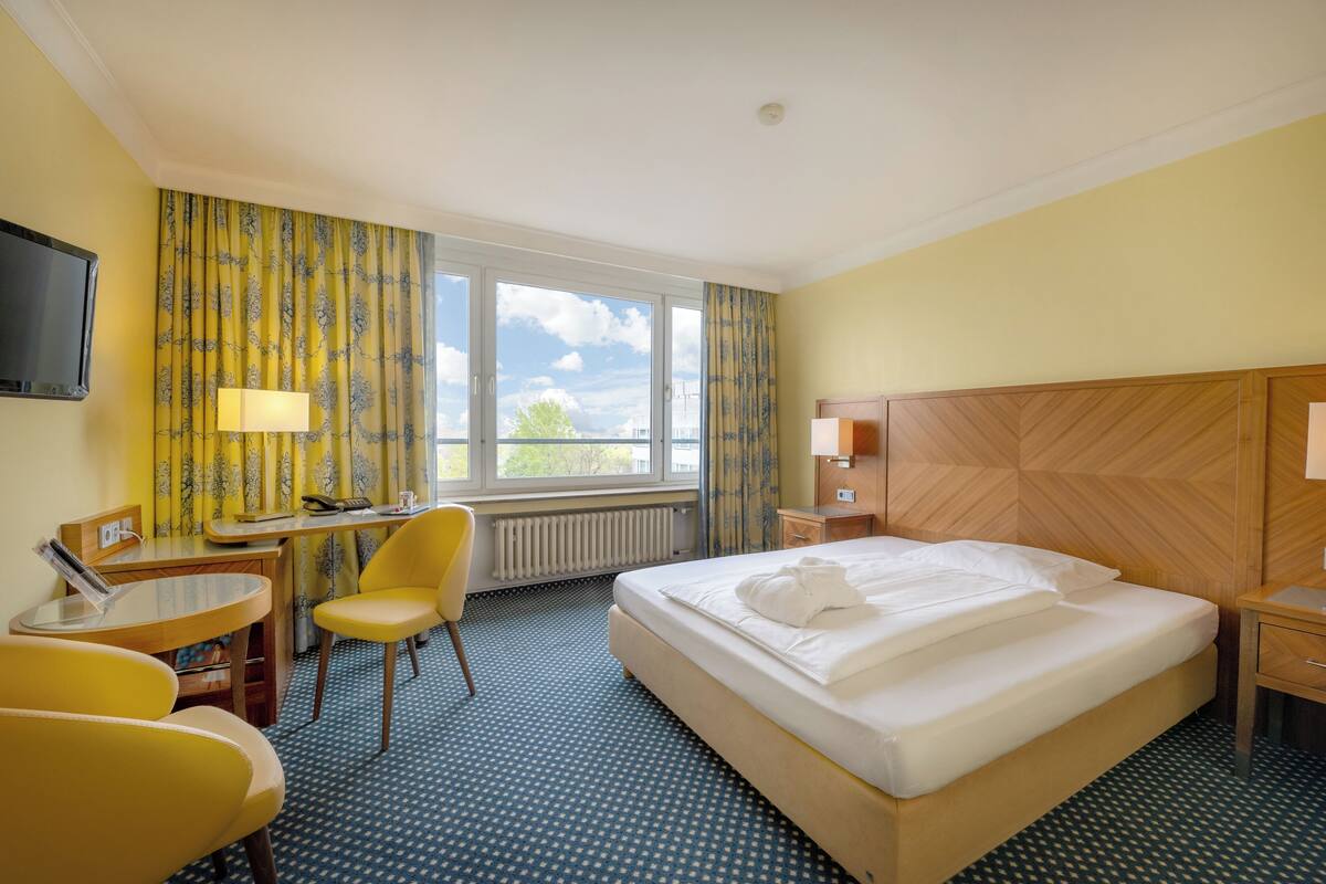 Ein Hotelzimmer mit Bett, Schreibtisch, Stuhl, Fernseher und einem fenster mit Vorhängen.