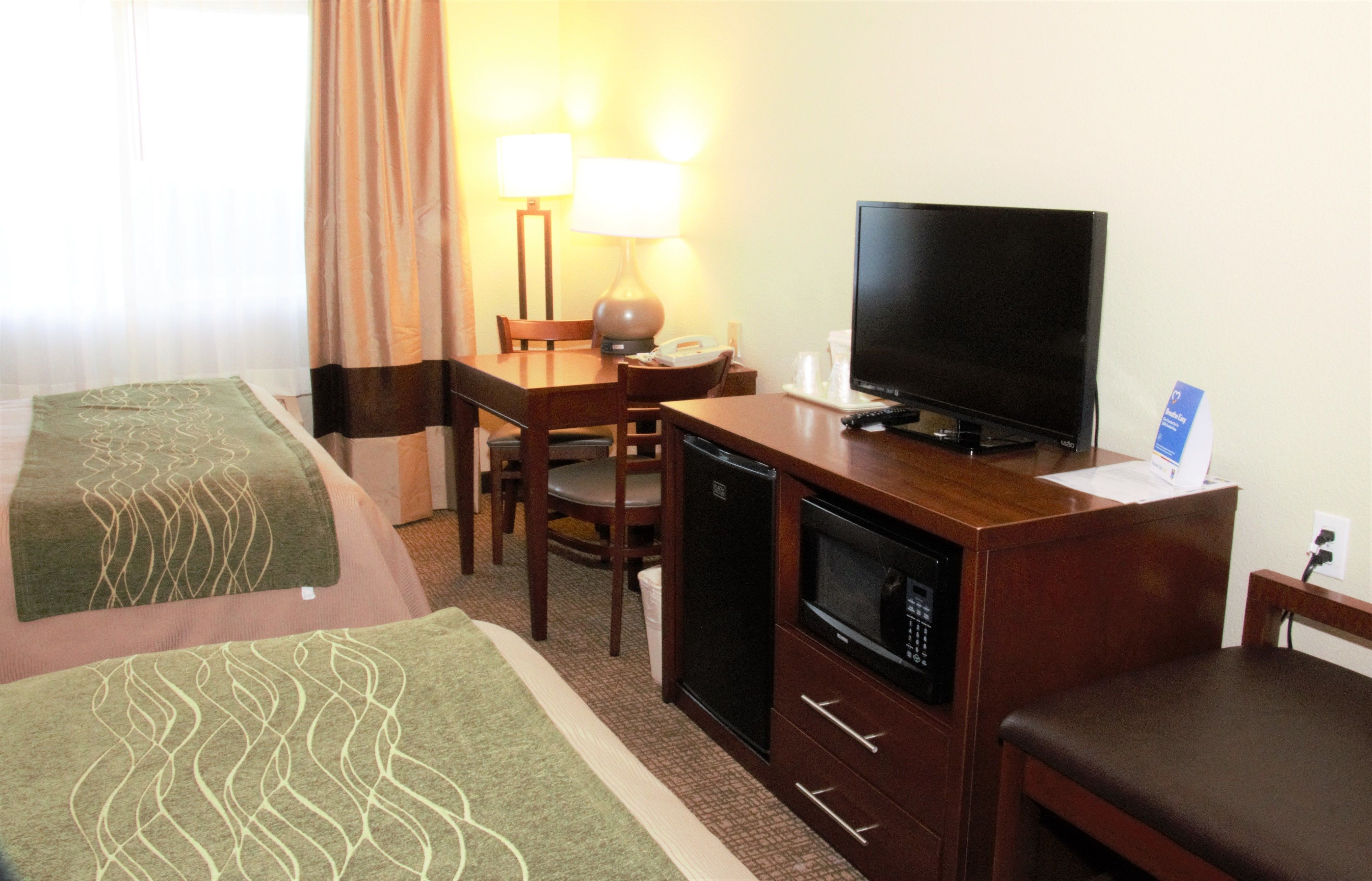 Una habitación de hotel con cama, escritorio con televisor, microondas y una silla.