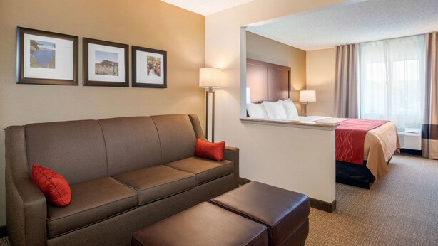 A hotel room with a sofa, a small table, a bed with a red blanket, a mirror, and three framed pictures on the wall.