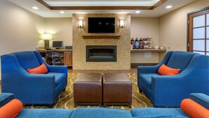 A hotel lobby with two blue armchairs, a fireplace, a flat-screen TV, and a bar area with bottles.