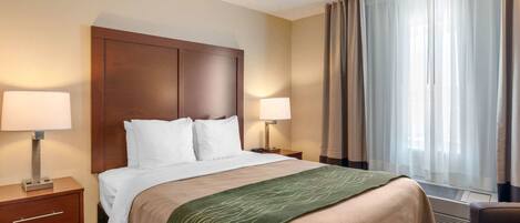 Une chambre d’hôtel avec un grand lit, deux tables de chevet avec des lampes, une fenêtre avec des rideaux et un climatiseur fixé au mur.