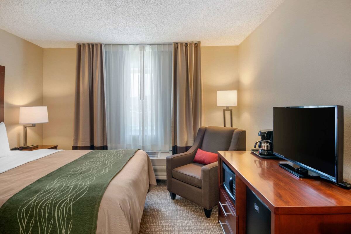 A hotel room with a bed, a desk with a television, a chair, and a coffee maker.