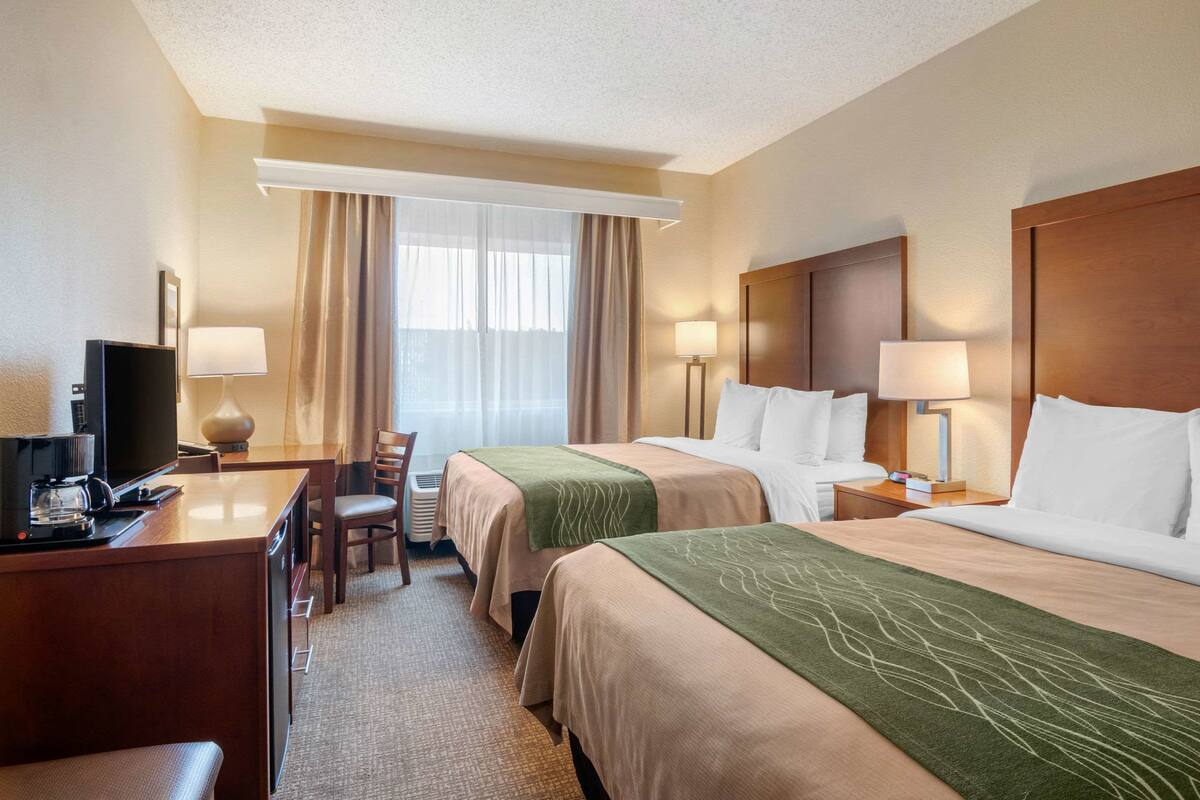 A hotel room with two beds, a desk with a TV, and a chair.