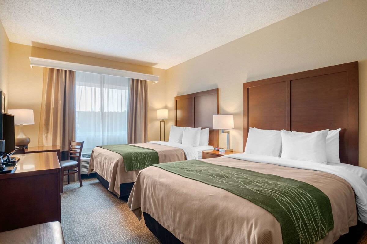 A hotel room with two beds, a desk, a chair, and a TV.