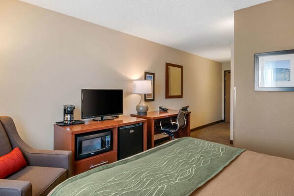 A hotel room with a bed, a desk with a television, a coffee maker, a microwave, and a chair.