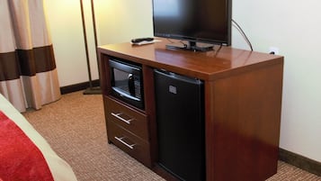 A compact hotel room with a wooden cabinet containing a microwave, a small refrigerator, and a flat-screen TV on top.