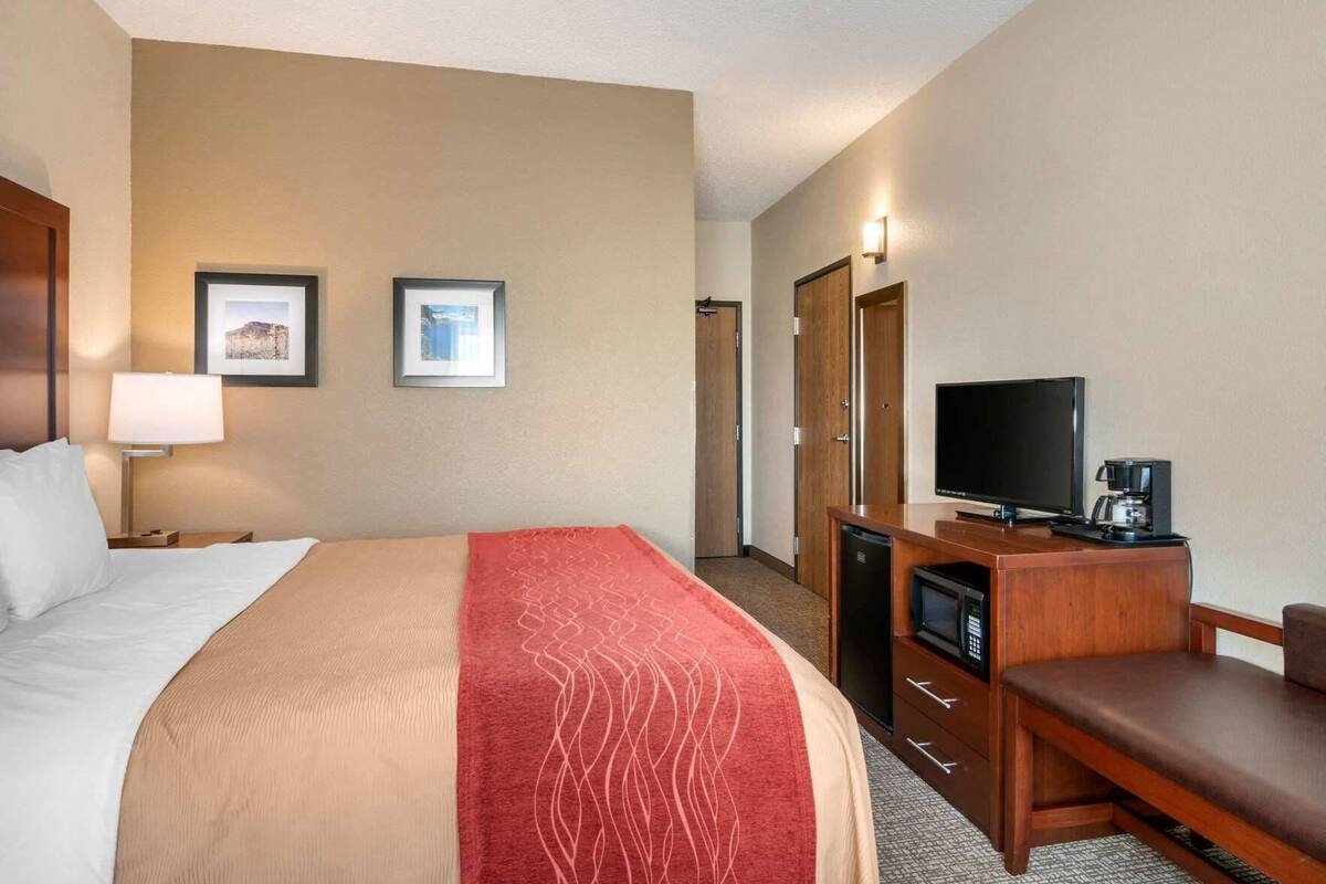 A hotel room with a bed, a desk with a television, a coffee maker, and two framed pictures on the wall.