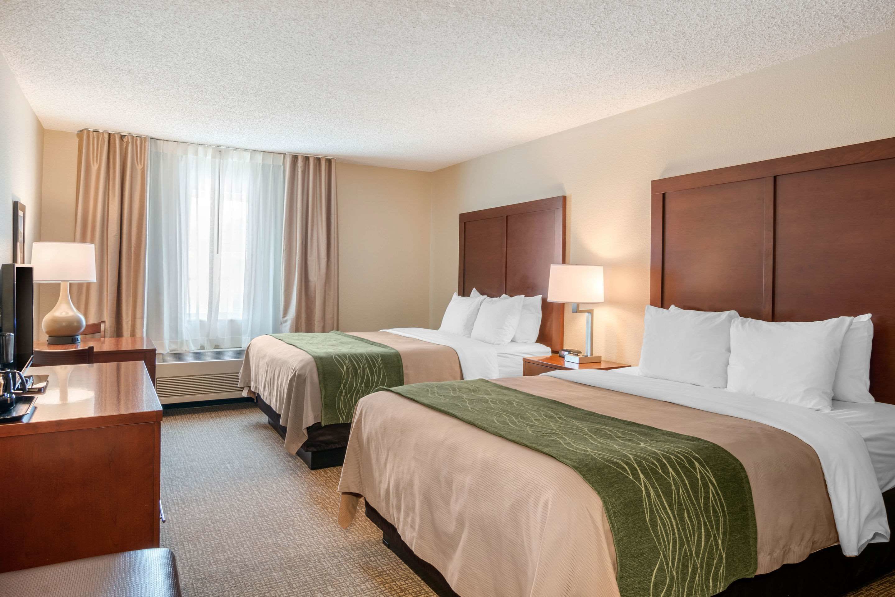A hotel room with two beds, a desk, and a TV.