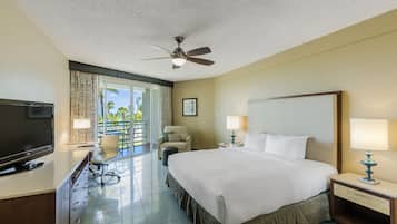 A hotel room with a bed, desk, TV, and a balcony with curtains.