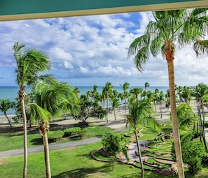 Un resort tropical con palmeras, un jardín cuidado y vistas al océano.