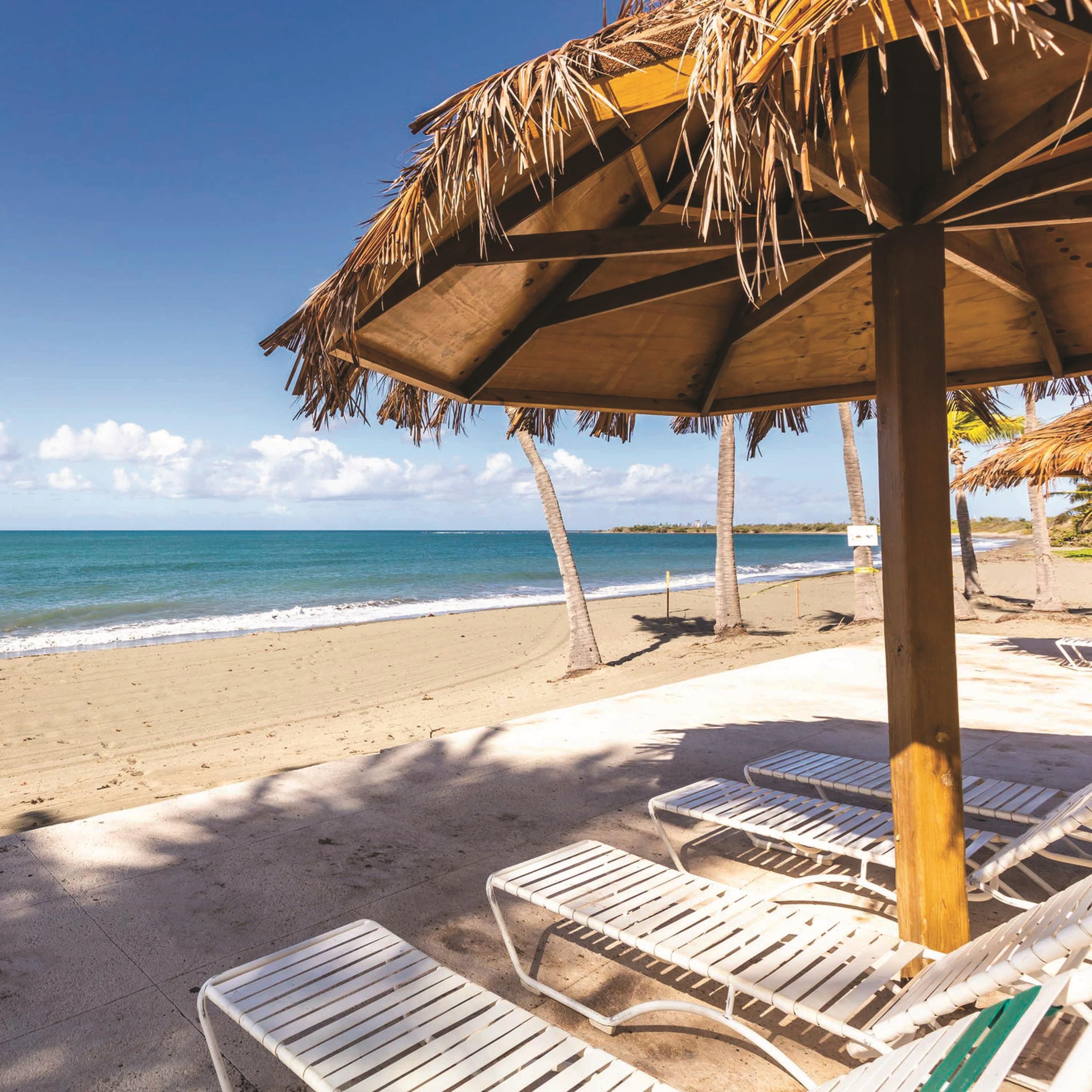 A beach with lounge chairs and a thatched umbrella.