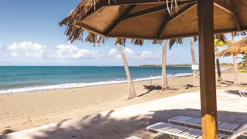 A beach with lounge chairs and a thatched umbrella.