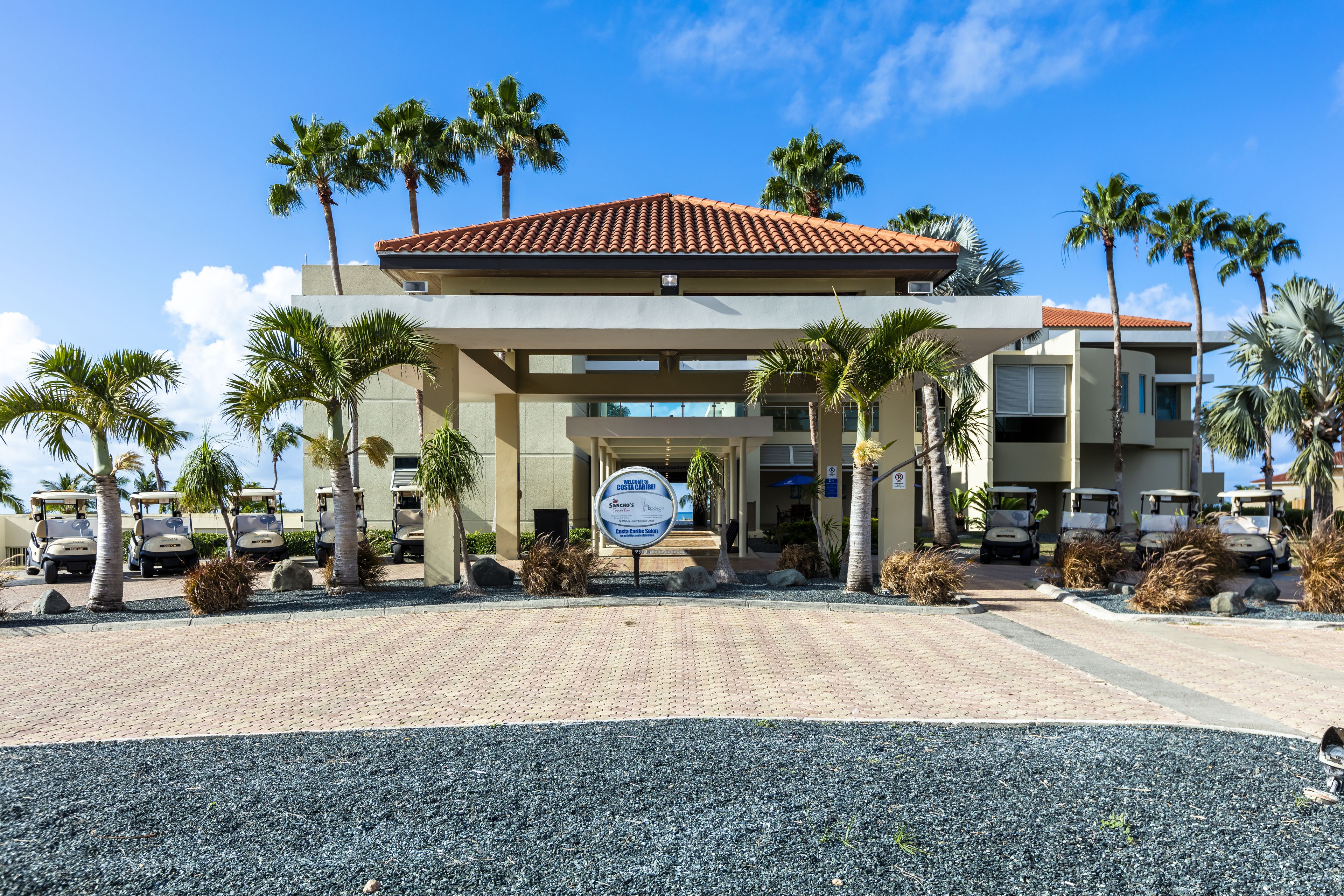 A hotel entrance with a sign, palm trees, and golf carts.