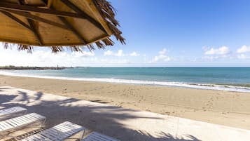 A beach with white lounge chairs, a wooden structure with a thatched roof, and a clear view of the ocean.
