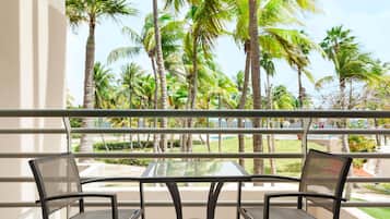 A balcony with a table and two chairs, overlooking a tropical garden with palm trees.