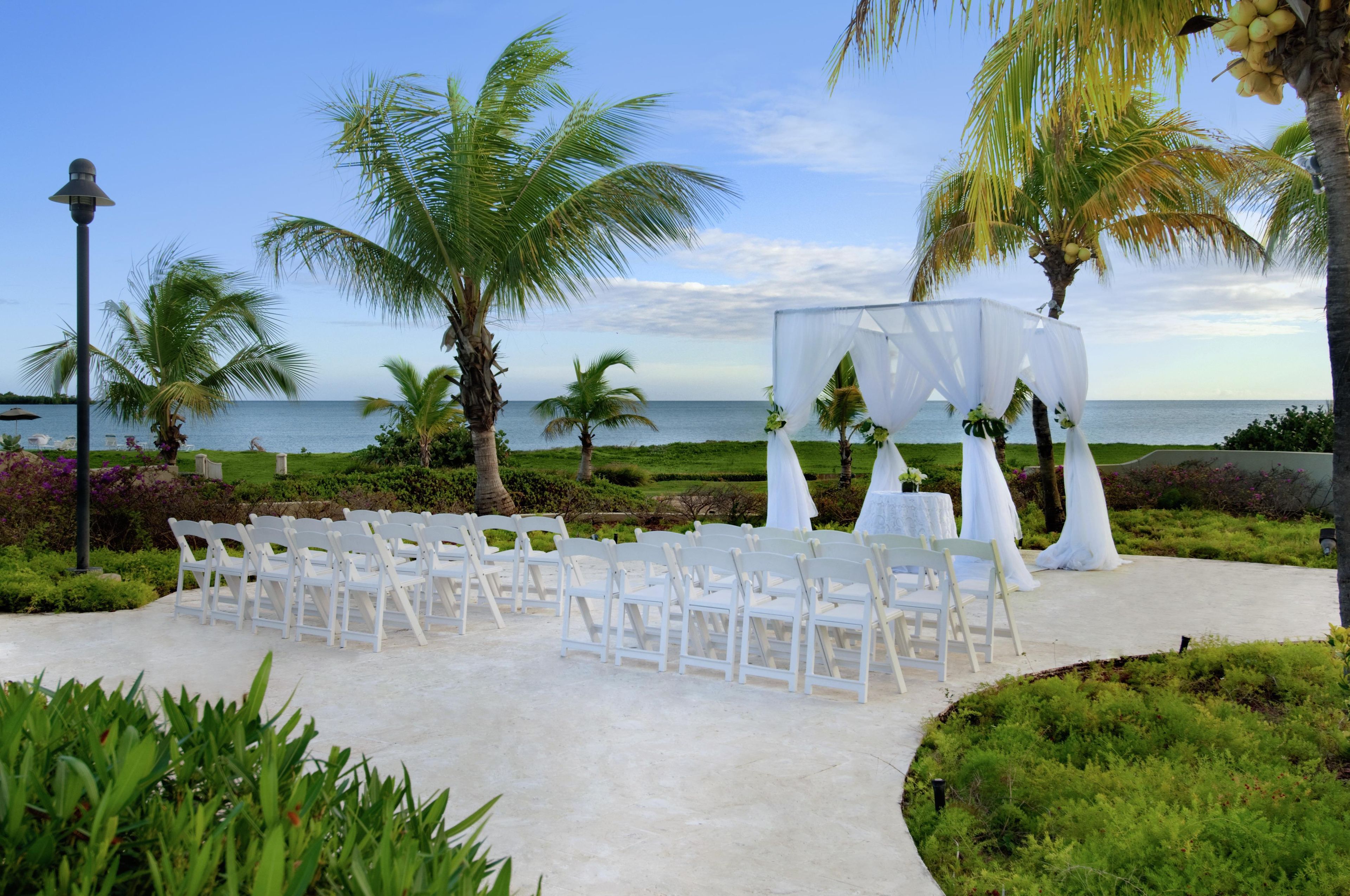 A beachside wedding setup with white chairs and a canopy.