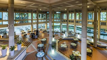 A spacious indoor area with multiple dining tables and chairs, large pillars, and a central water feature.