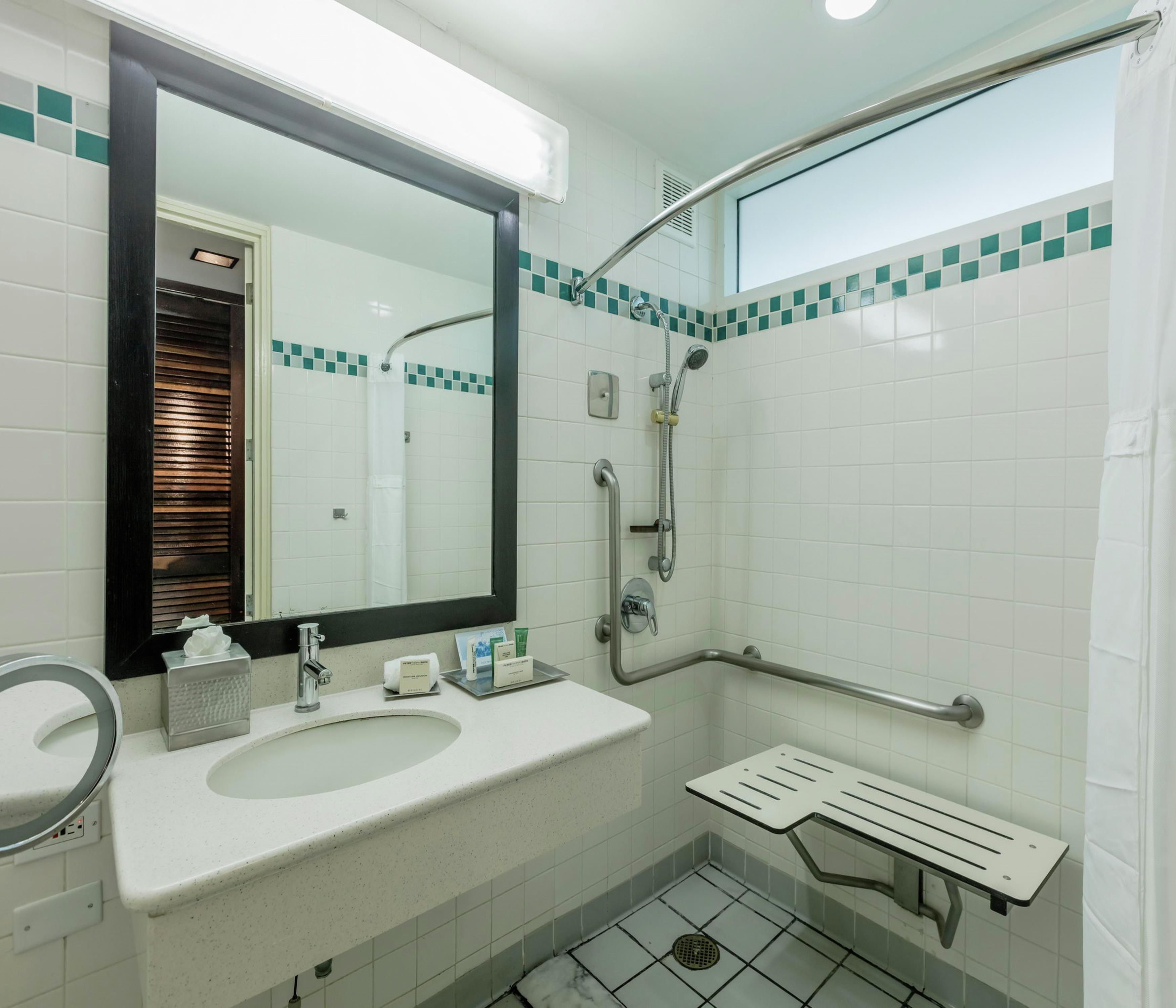 Une salle de bain équipée d’un lavabo, d’un miroir, d’une douche et d’une barre d’appui.