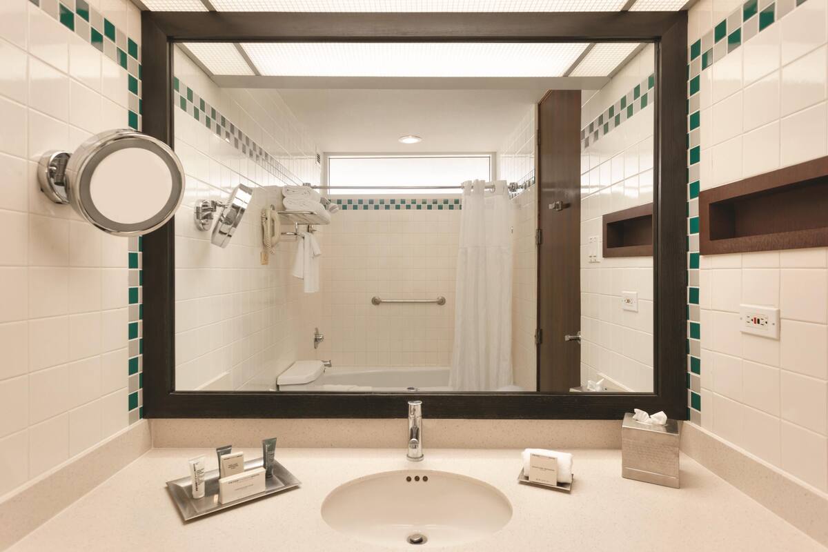 Un baño con un espejo grande, un lavamanos, un perchero para toallas y una zona de ducha.