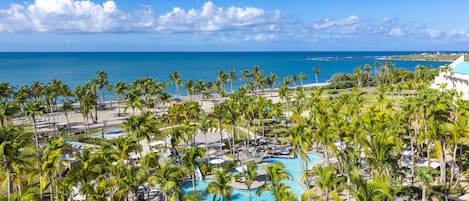 A resort with a swimming pool surrounded by palm trees, a beach, and a view of the ocean.