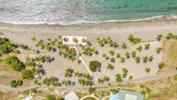 Vue aérienne d’une plage avec des palmiers, un sentier et un petit espace piscine.