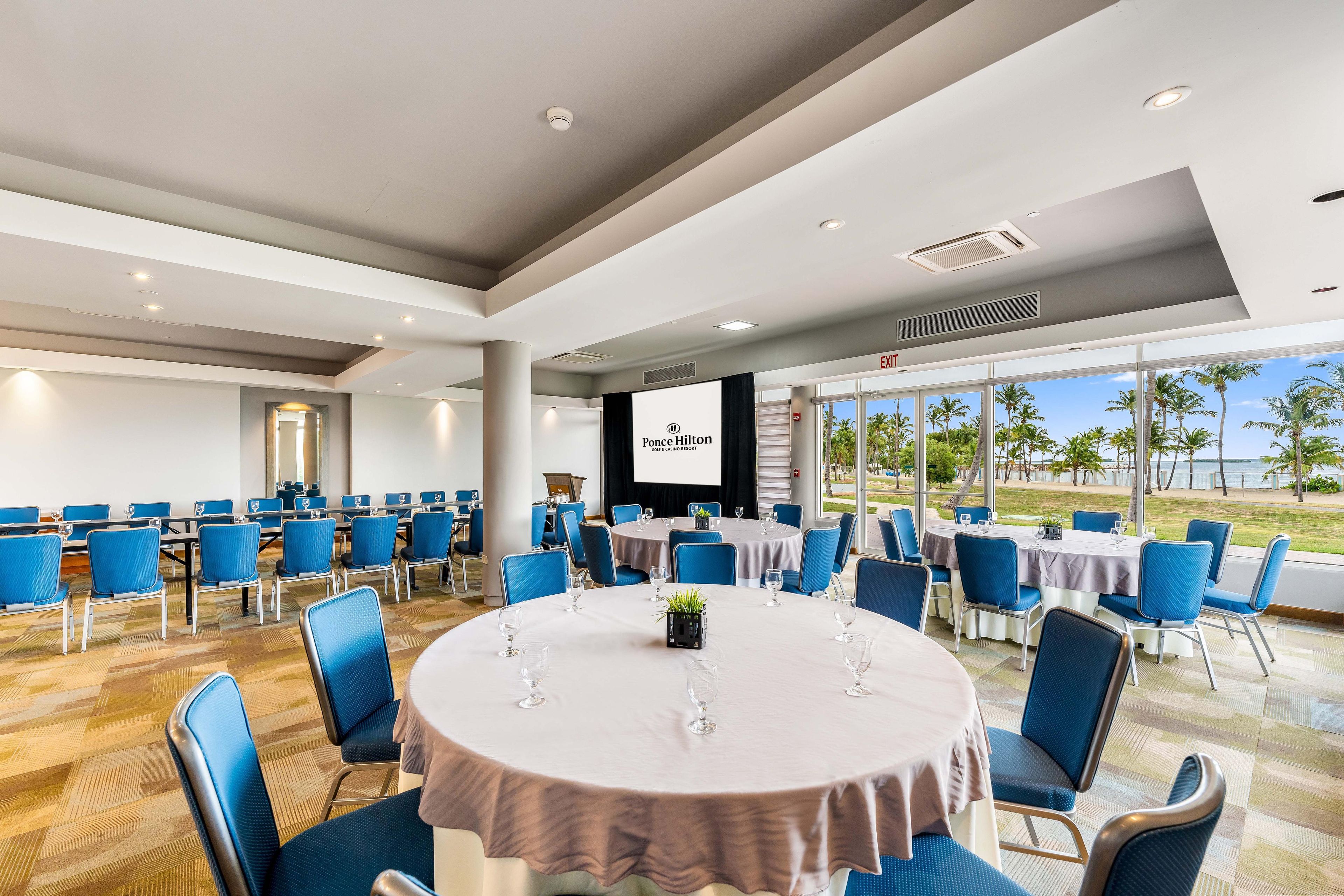 A conference room with round tables, blue chairs, and a large screen for presentations.