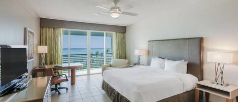 A hotel room with a bed, desk, chair, and a view of the ocean.
