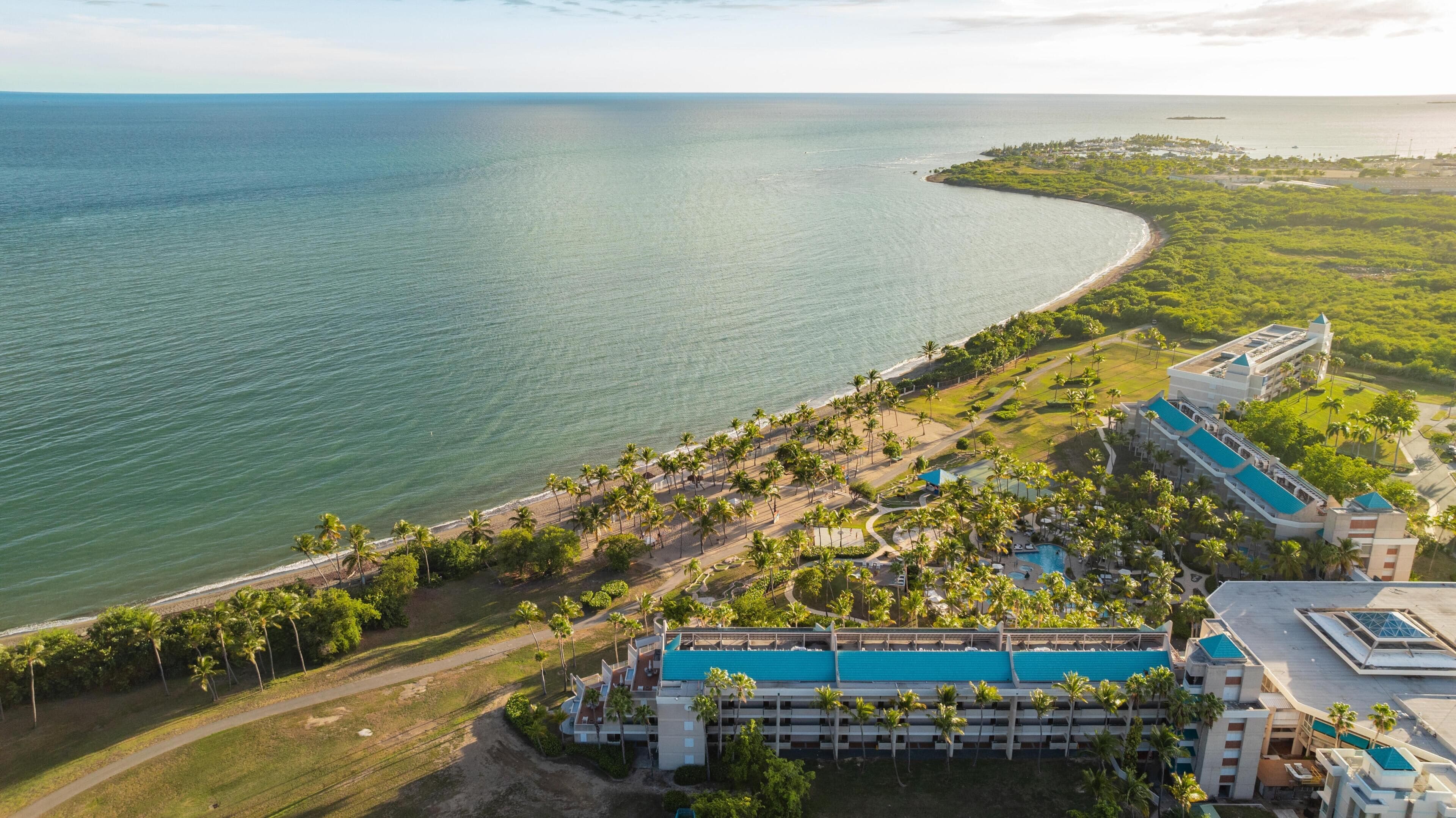 Vue aérienne d’un complexe hôtelier avec une plage, une piscine et un grand bâtiment doté d’un toit bleu.