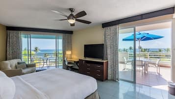 Habitación de hotel con cama, escritorio, televisor y balcón con vista al océano.