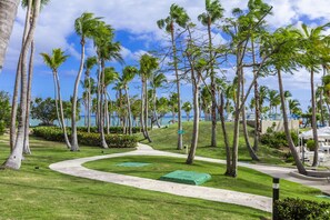 A pathway winding through a tropical garden with palm trees and a view of the ocean. - Hilton Ponce Golf & Casino Resort (Ponce)