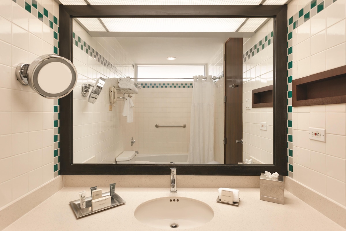 A bathroom with a large mirror, a sink, a towel rack, and a shower area.