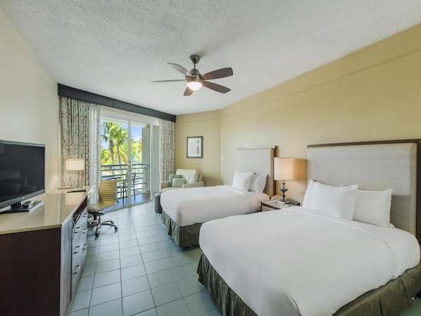 A hotel room with two beds, a desk with a TV, a ceiling fan, and a balcony with curtains. - Hilton Ponce Golf & Casino Resort (Ponce)