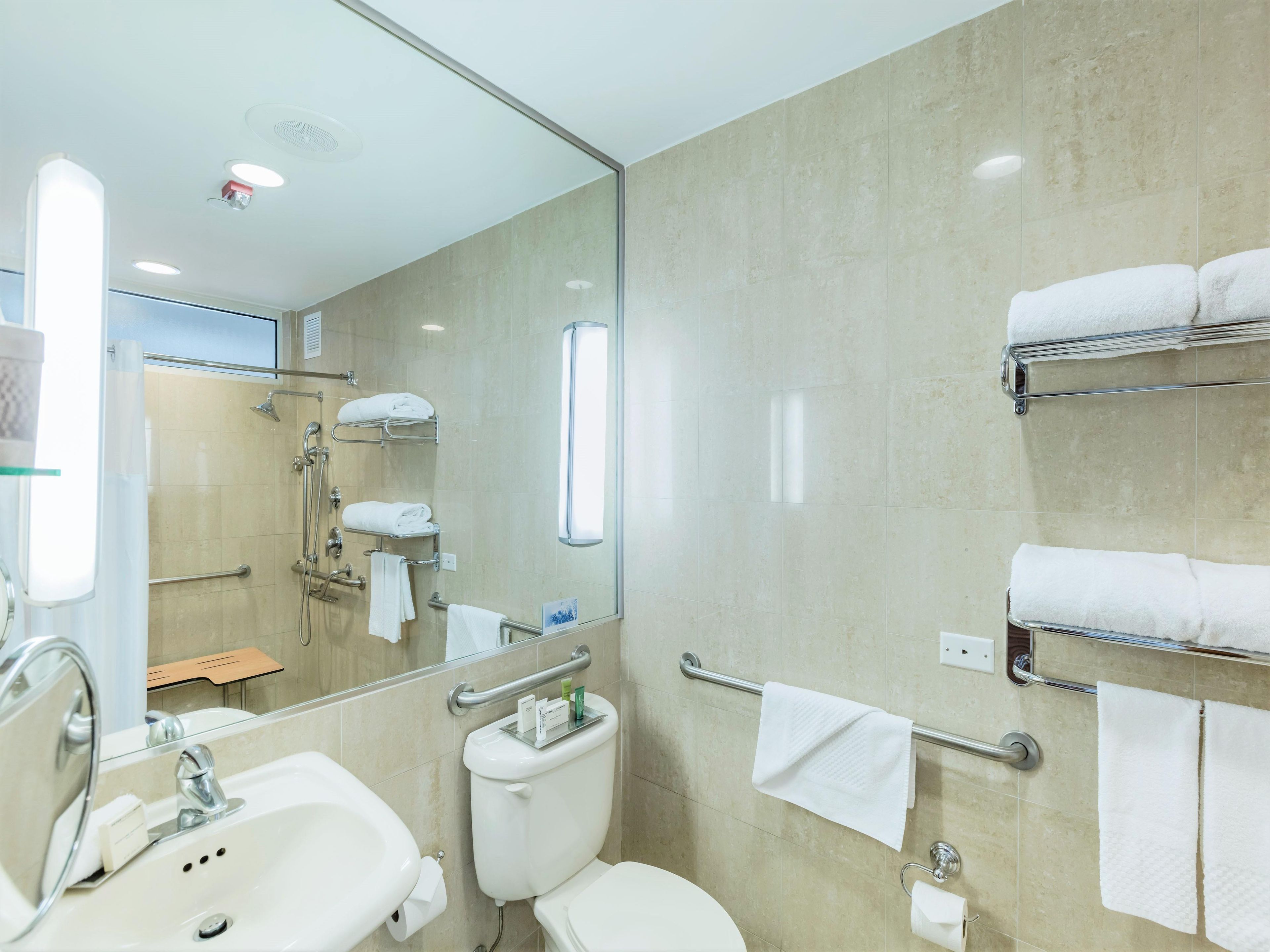 Un baño moderno con lavamanos, inodoro y ducha. Hay varios toalleros y un box de ducha de vidrio.