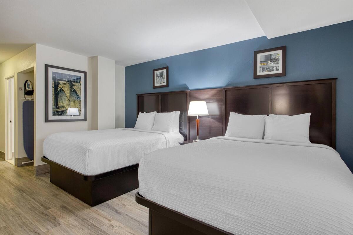 A hotel room with two beds, a nightstand with a lamp, and framed pictures on the wall.