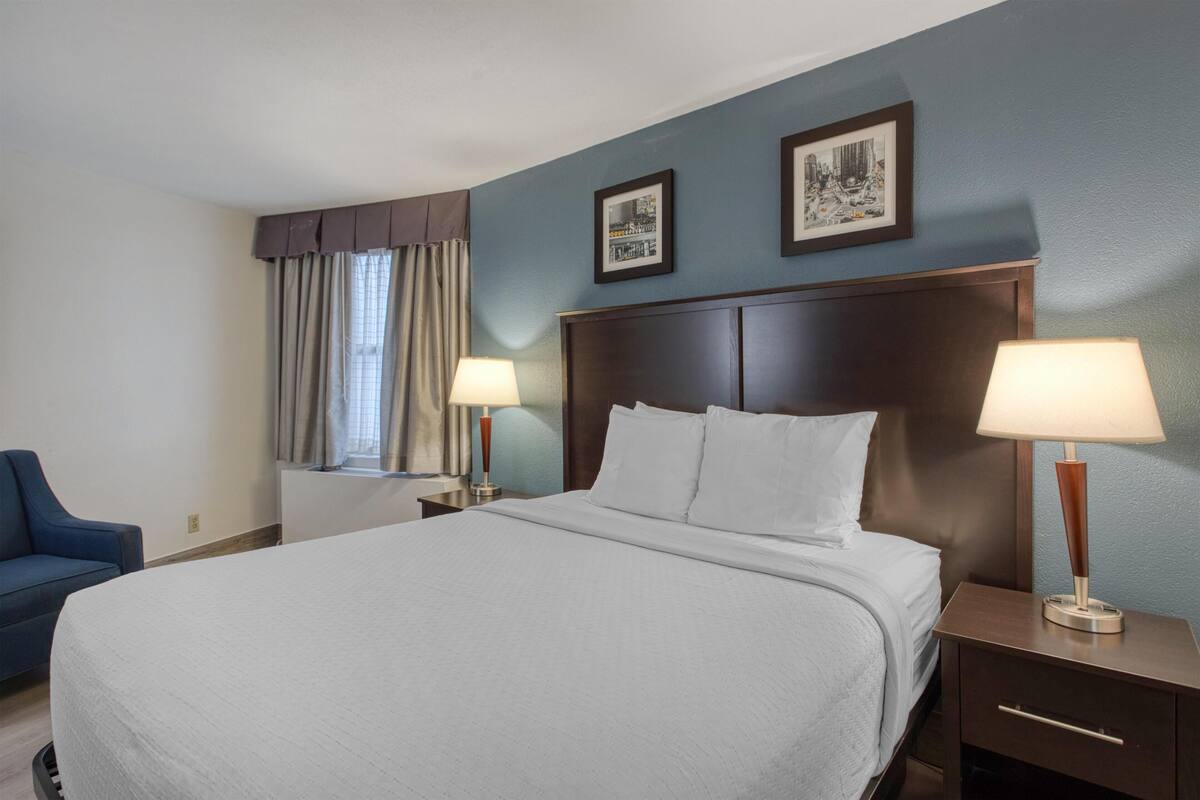 A hotel room with a large bed, two bedside tables with lamps, a chair, and a window with curtains.