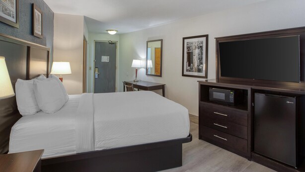 A hotel room with a bed, bedside tables, a desk, a microwave, a refrigerator, and a flat-screen TV. - Best Western Gregory Hotel (Brooklyn)