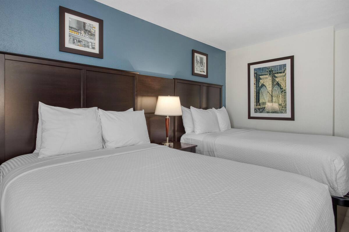 A hotel room with two beds, a nightstand with a lamp, and framed pictures on the walls.