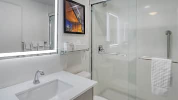 A modern bathroom with a glass shower enclosure, a white sink, and a large mirror.
