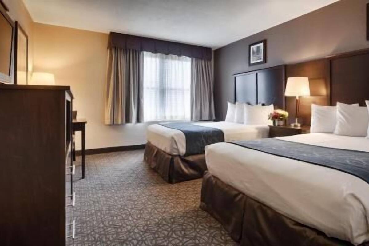 A hotel room with two beds, a desk, a lamp, and a picture on the wall.