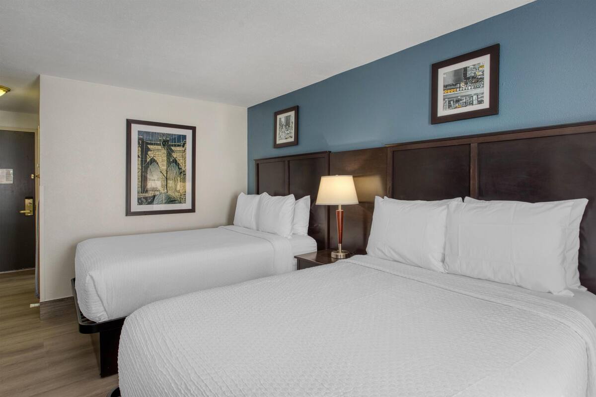 A hotel room with two beds, a nightstand with a lamp, and framed pictures on the wall.