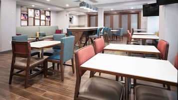 Un restaurant avec des tables et des chaises en bois, un canapé et un téléviseur fixé au mur.