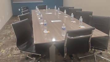 Un salón de conferencias con una larga mesa, sillas, botellas de agua y una pantalla de proyector.
