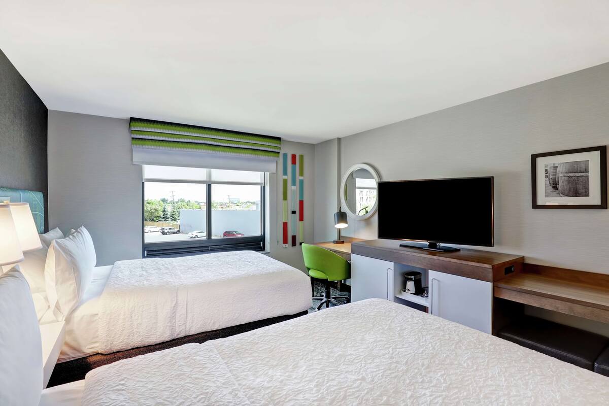 Habitación de hotel con dos camas, un escritorio, televisor y ventana con vista al exterior.
