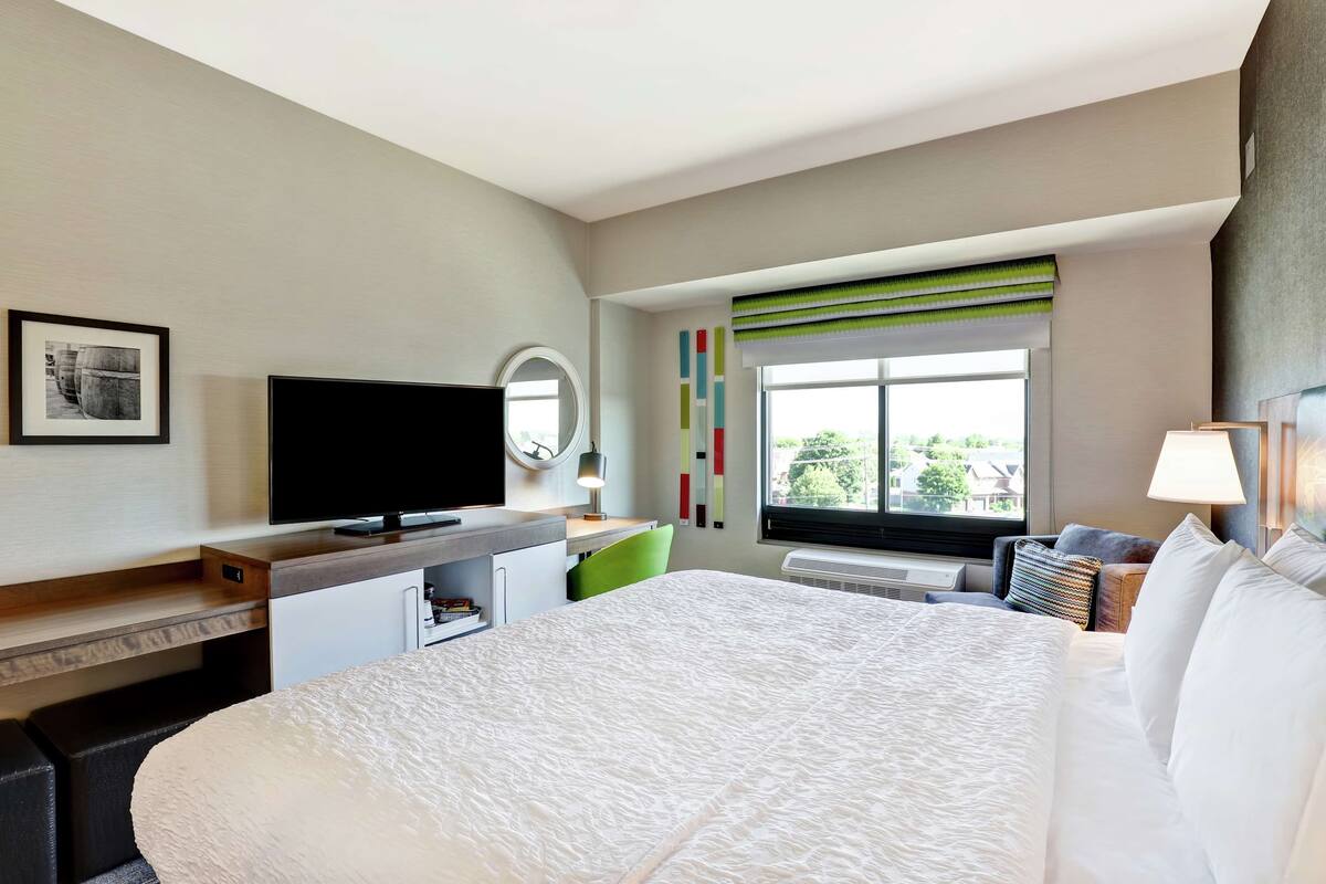 Habitación de hotel con una cama grande, un escritorio con televisión de pantalla plana, una silla, una ventana con vistas y una mesita de noche con lámpara.