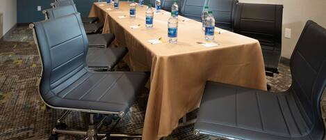 Un salón de conferencias con una mesa larga, varias sillas y botellas de agua sobre la mesa.