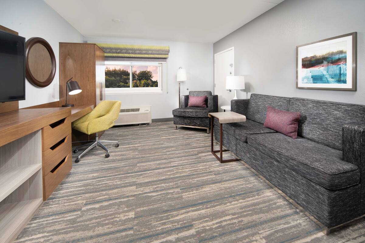 Una sala de estar moderna con un sofá gris, una silla amarilla y un televisor sobre un mueble de madera.