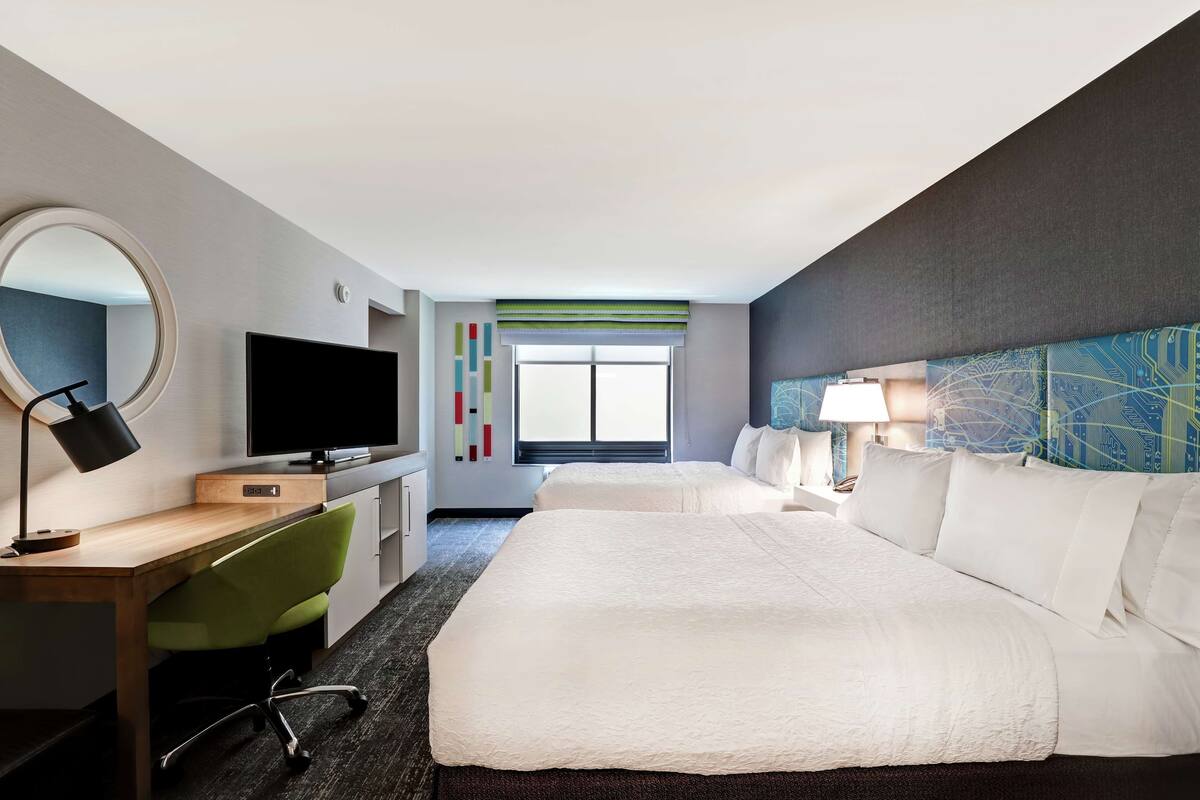 Habitación de hotel con cama, escritorio con silla, televisor, espejo y ventana con vistas.